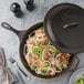 A Lodge cast iron skillet with vegetables and onions cooking in it on a table.