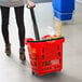 A woman pushing a Regency red plastic shopping basket with wheels full of groceries.