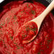 A bowl of red sauce with a wooden spoon.
