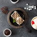 A Lodge cast iron grill pan with food including ice cream and marshmallows on a table.