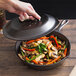A Lodge cast iron skillet with a lid cooking vegetables and mushrooms.