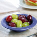 A Carlisle Ocean Blue rimmed melamine fruit bowl filled with red and green grapes on a table.