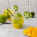 Two glasses of yellow liquid garnished with lime and jalapeno slices on a marble counter.