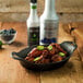 A bowl of chicken wings with jalapenos on top on a wooden table with a bottle of Monin Jalapeno Concentrated Flavor.