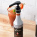 A bottle of Monin Habanero Concentrated Flavor on a counter next to a glass of liquid.