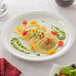 A plate of ravioli with tomatoes and green sauce on top.