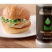 A sandwich on a plate with a roll next to a bottle of Monin Basil Concentrated Flavor.