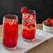 Two glasses of red strawberry drinks with ice and strawberries on a white plate.