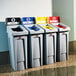 A row of Rubbermaid Slim Jim recycling bins with white rectangular lids labeled for paper and bottles.
