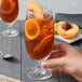 A hand holding a glass of iced tea with lemon slices and a peach slice.