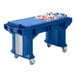 A blue Cambro Versa work table with heavy duty casters and a blue plastic bin filled with bottles on it.