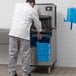 A man in a white coat using a blue scoop to pour ice into a Manitowoc air cooled ice machine.