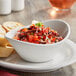 An Acopa white porcelain bowl filled with salsa on a table with bread and crackers.