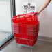A hand pulling a stack of red Regency shopping baskets.