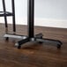 A Lancaster Table & Seating black cast iron bar height table leg on a wood floor.