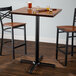 A Lancaster Table & Seating black cast iron bar height table base with two chairs and a glass of beer on a wood floor.