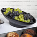 A G.E.T. Enterprises black resin-coated aluminum bowl filled with grapes and muffins on a table in a hotel buffet.