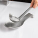A hand holding a ladle over a stainless steel spoon rest.