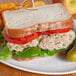 A sandwich on a plate with lettuce, tomato, and a toothpick, made with Bumble Bee Chunk Light Tuna.