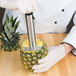 A person using a Choice stainless steel pineapple slicer to cut a pineapple.