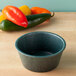 A HS Inc. jalapeno ramekin on a table next to red peppers.