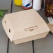 A Bagcraft corrugated take-out box on a yellow surface with a fork and knife on it.