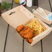 A Bagcraft corrugated take-out box of chicken and fries on a table.