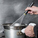 A hand using a Matfer Bourgeat stainless steel whisk to stir food in a pot.