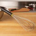 A Matfer Bourgeat stainless steel whisk with an Exoglass handle on a wooden surface.