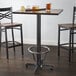 A Lancaster Table & Seating bar table with a metal base and FLAT Tech table levelers with glasses of beer on it and two chairs.