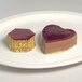 A stainless steel hexagon mold next to two pieces of chocolate and a heart shaped pastry.