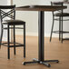 A Lancaster Table & Seating black cast iron bar height table base with self-leveling feet under a bar table with plates on it.