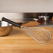 A Matfer Bourgeat stainless steel whisk on a cutting board.