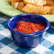 A navy blue Thunder Group smooth melamine ramekin filled with red sauce on a table with french fries.