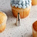 A cupcake with ruffled frosting made using an Ateco ruffle piping tip on a table with more cupcakes.