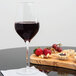 A Stolzle Exquisit Royal wine glass filled with red wine next to food on a cutting board.
