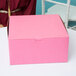 A woman holding a pink 10" x 10" x 5" cake box with a bow on it.