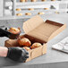 A person in gloves holding a brown muffin in a Kraft pie box.