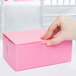 A hand holding a pink bakery box with a pink ribbon.