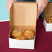 A person holding a white bakery box filled with muffins.