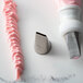 A metal Ateco basketweave piping tip on a white surface with a pastry bag and pink frosting.