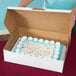 A person opening a white half sheet cake box to reveal a cake with frosting and sprinkles.