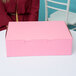 A woman sitting at a table with a pink 14" x 10" x 4" cake box on it.
