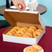 A 12" x 12" white bakery box filled with donuts on a table.