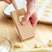 A person using a Fox Run beech wood gnocchi board to make gnocchi on a wooden surface.