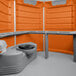 A grey and orange PolyJohn wheelchair accessible portable toilet.