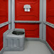 A PolyJohn wheelchair accessible portable restroom with red and grey walls.