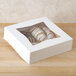 A 9" x 9" white bakery box with a transparent window holding pastries.