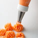 A person using an Ateco drop flower piping tip to pipe orange flowers over orange frosting.