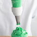 A person using an Ateco Drop Flower piping tip to decorate a cupcake with green frosting.
